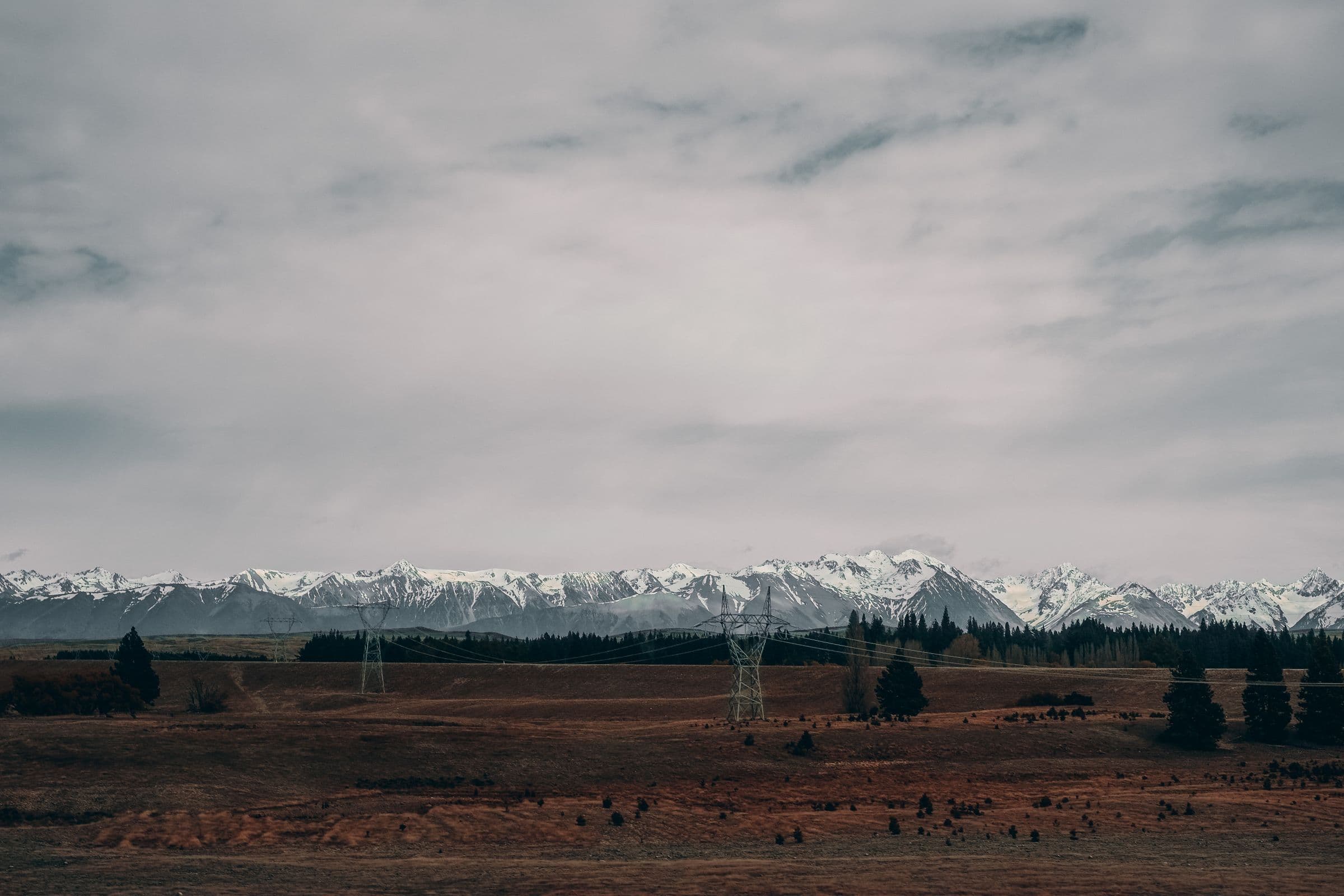 Transmission towers crossing open range beneath snow-capped peaks.