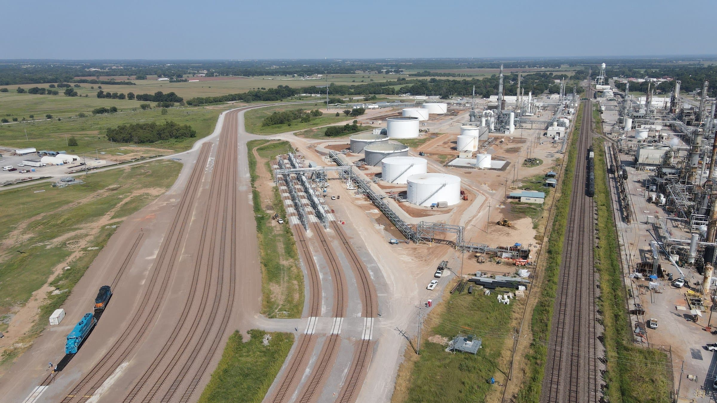 Aerial view of a rail transloading terminal with loading racks, storage tanks, and a switcher locomotive.