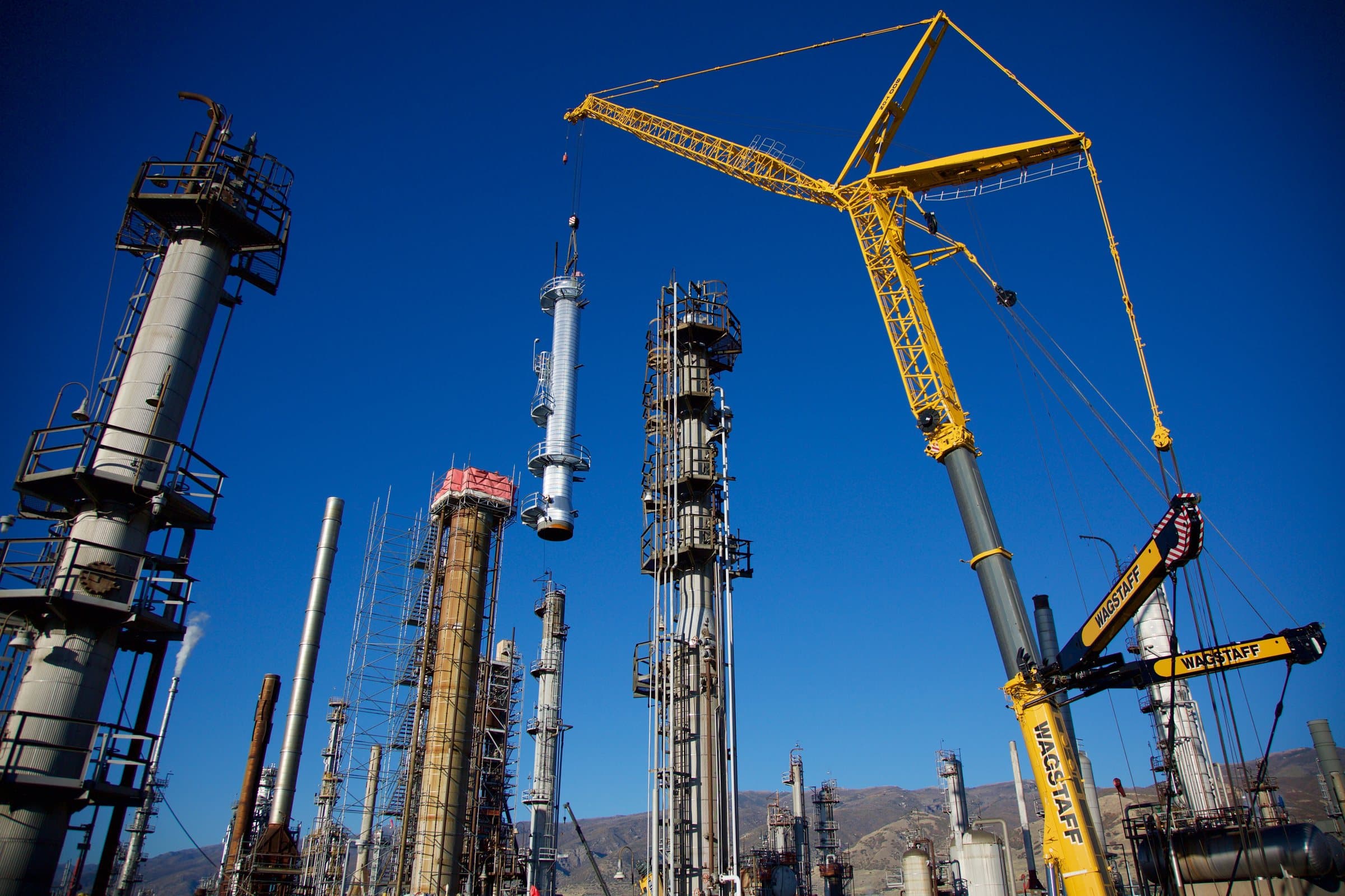 A crawler crane setting a process column at a refinery, with the Wasatch front behind it.